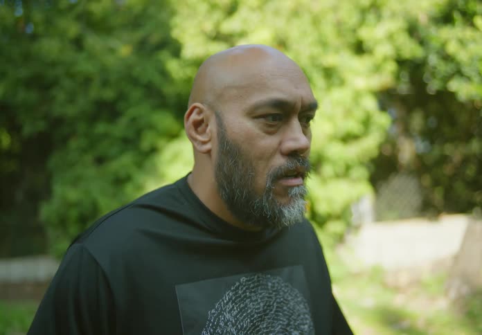 A black man stands outdoors while talking