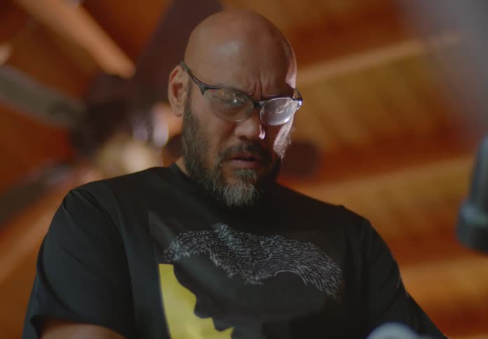A tan man with bald head and beard is wearing safety glasses and is intently focused on something below him.