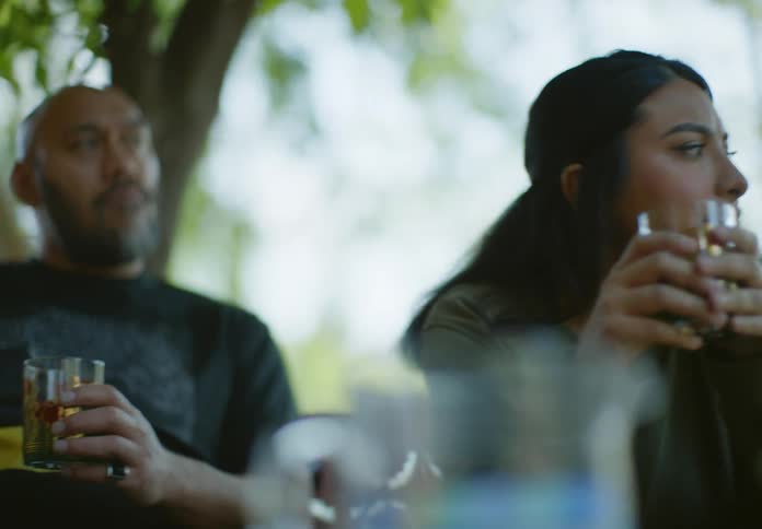A man and a woman sit on a porch relaxing while having drinks together