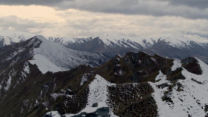 Revealing a range of mountains that are partially covered in snow and the sky is filled with heavy white clouds