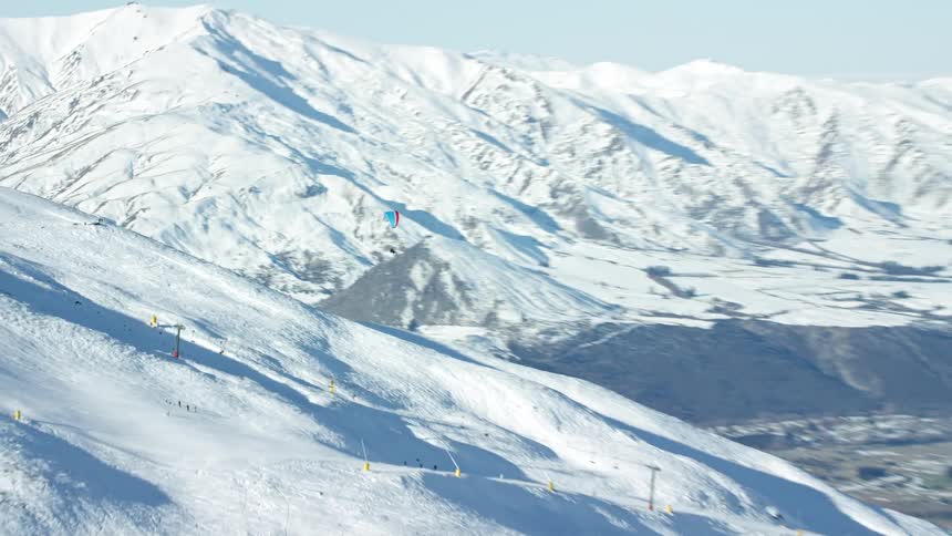 Aerial view of a snowy mountain slope with skiers and a paraglider