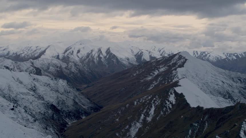 Aerial view of a mountain range covered in snow under an overcast sky