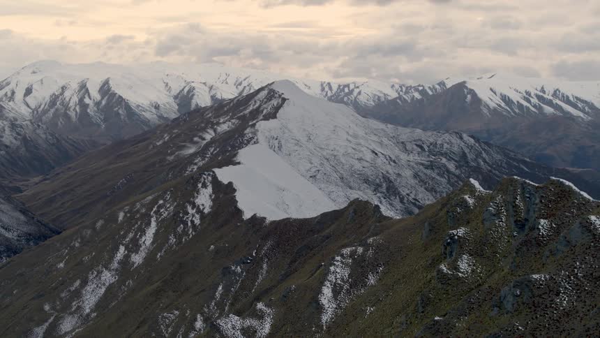 The top of a mountain that is half native grass and half covered in ice and snow in a mountain range