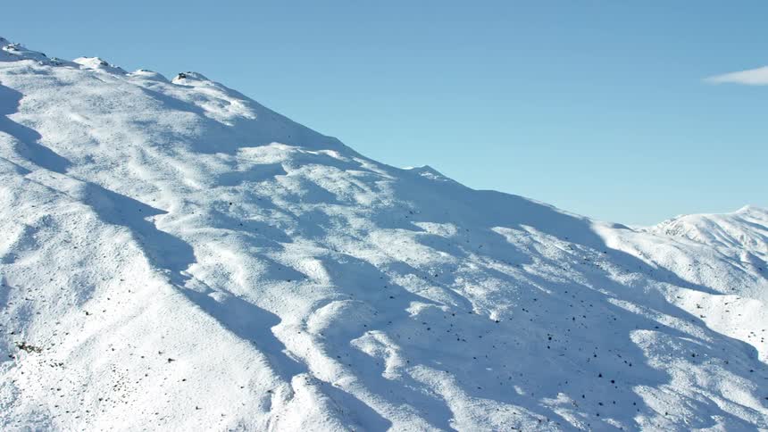 Aerial view of snowcovered hills with exposed rocky surfaces under a clear blue sky