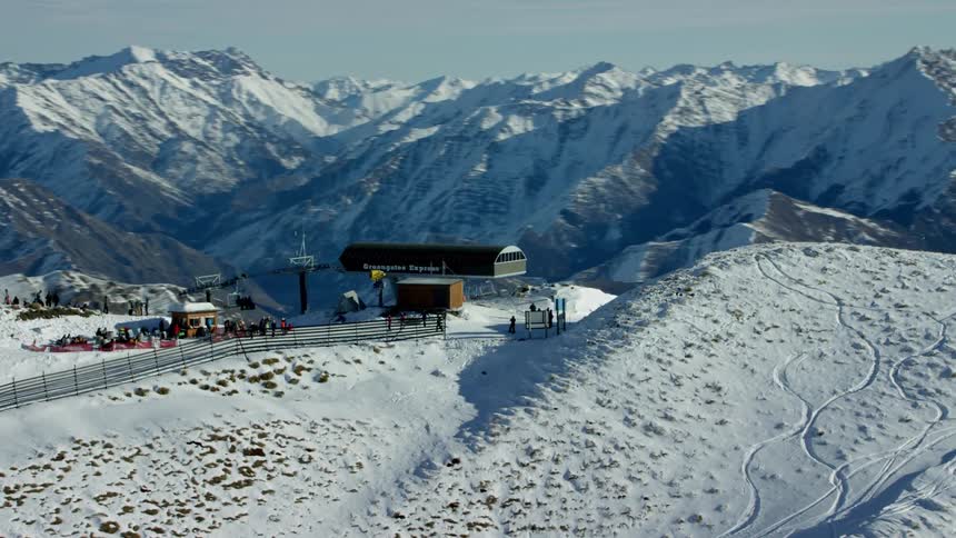 Chairlift at the top of a ski resort with people skiing on the slope