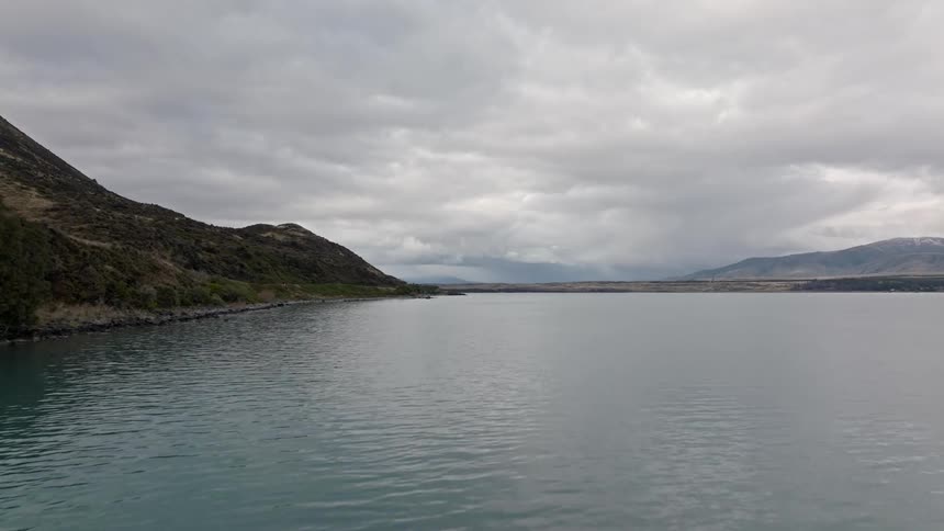Small waves flow past mountain bordering water on an overcast day