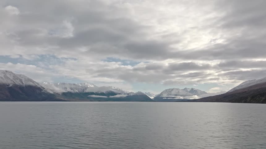 Aerial view of a tranquil lake with mountains in the background partially obscured by clouds