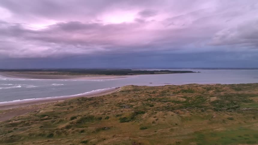 Coastal landscape under a dramatic sky with shades of purple