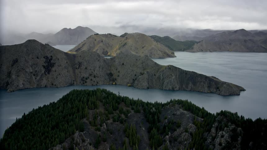 A tranquil lake with multiple islands surrounded by rugged hills under a cloudy moody sky