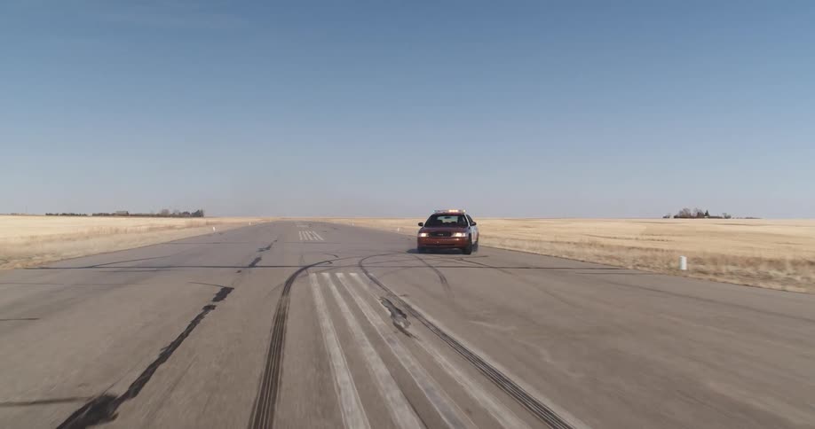 A red police car brakes and spins on an empty tarmac in the countryside