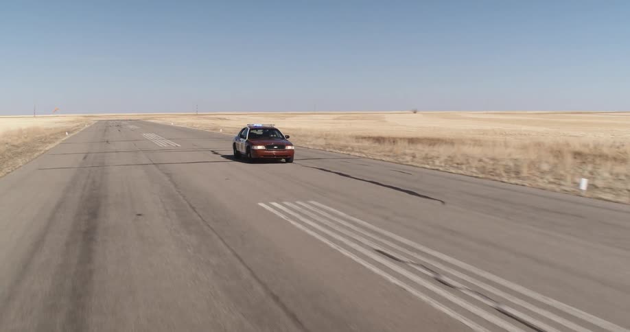 A police car speeding along a wide asphalt street in a desert region