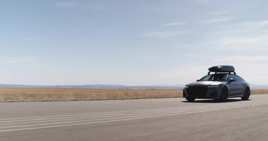 A car drives down a wide swath of pavement in a rural area