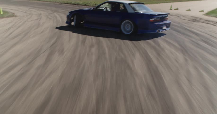 A blue sports car drifts on a track leaving tire marks on the asphalt