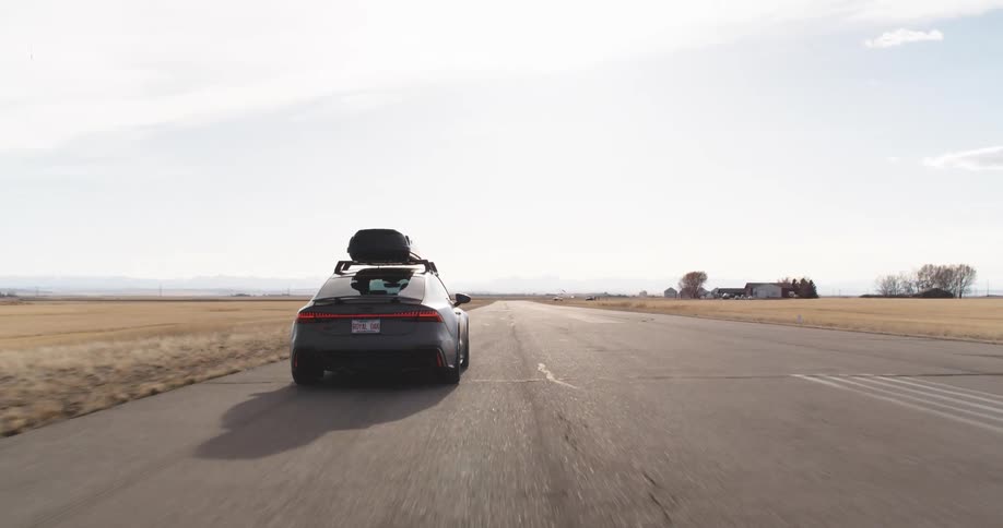 A sports car with a luggage on top driving on an asphalt road in a desert region