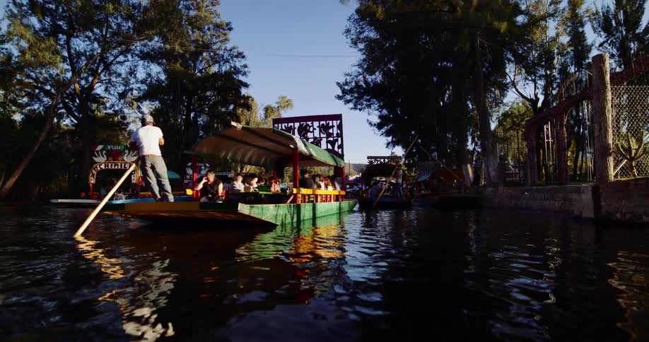 Several people in a boat with one person at the end using an oar that goes to the bottom of the river