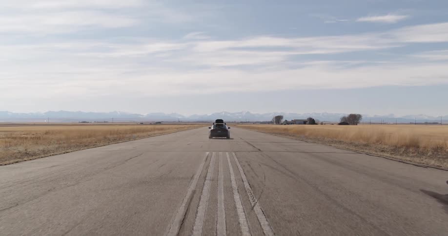 Gray sports car speeding on an empty road with open fields