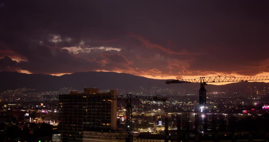 A cityscape at dusk with a construction crane silhouette in the foreground under a purple and orange sky
