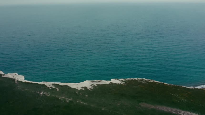 Coastal landscape where a vast body of water meets a green landmass with white cliffs