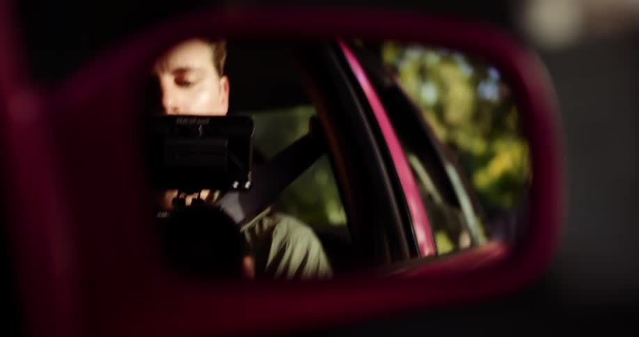 A man films himself via the cars side mirror while he drives