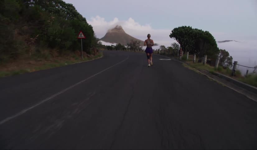 A woman is running on a road in front of trees and mountains