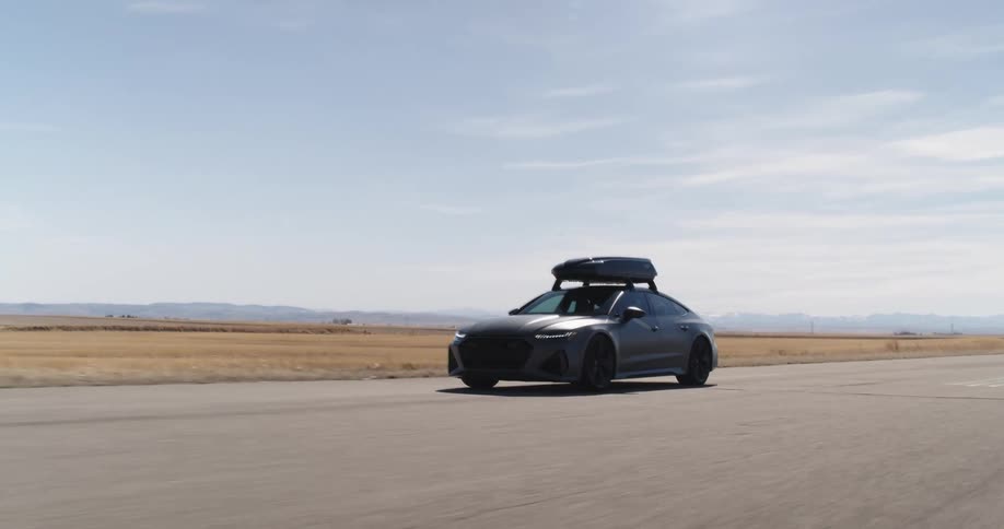 A car carrying a boat on the roof drives on the road in a desolate grassland