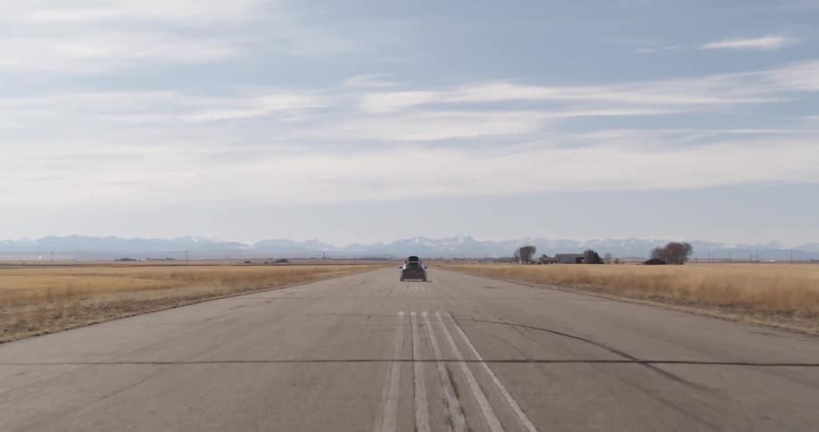 Gray car with luggage on the roof speeding down an airport runway