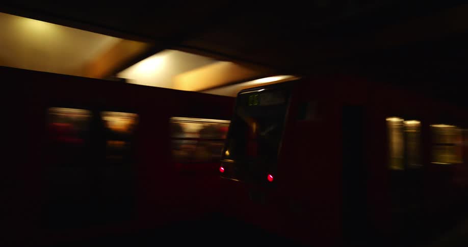 A dimly lit subway station with a red train passing through