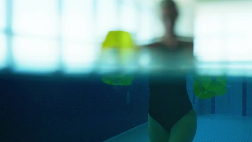 A woman exercises on an indoors swimming pool using weights