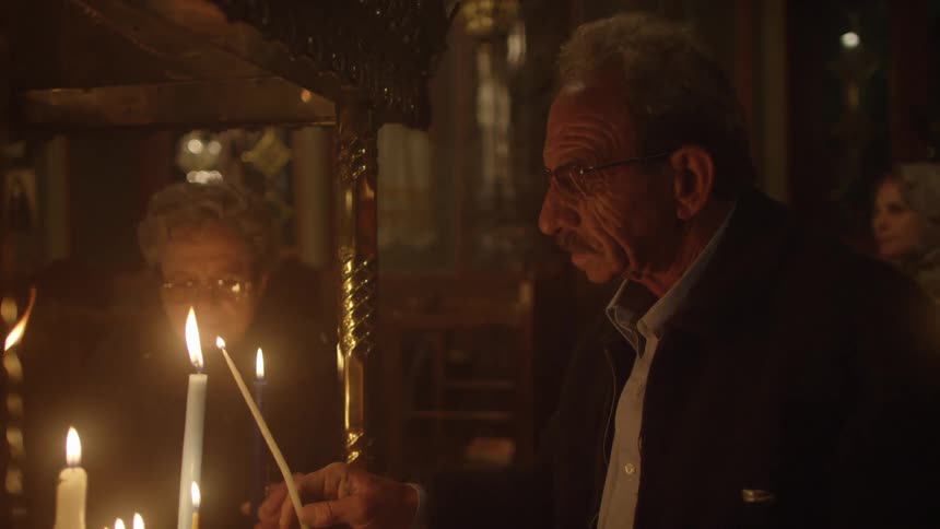 An elderly couple light candles in a church