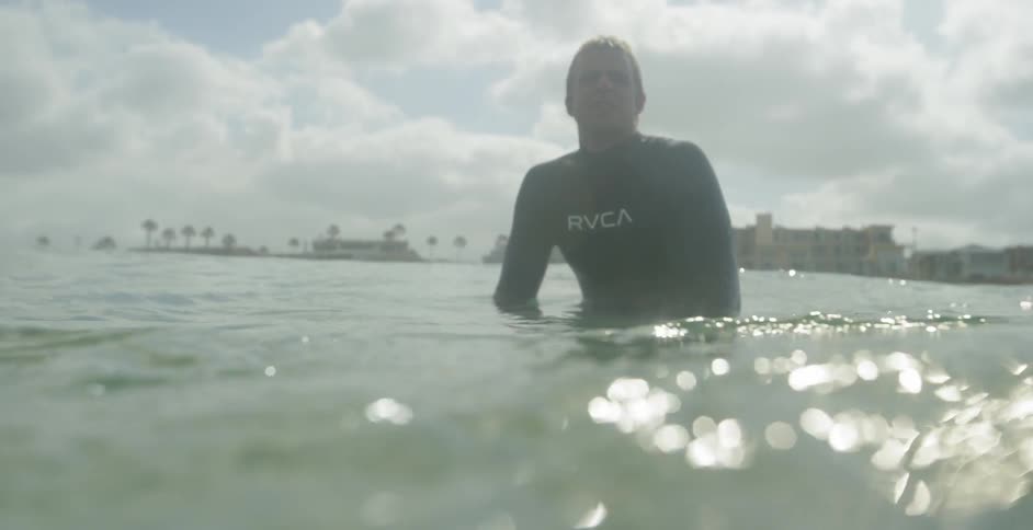 Surfer floating in swaying ocean water on cloudy day
