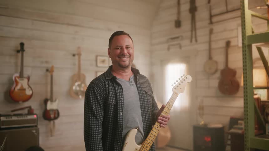 A man is smiling while holding a guitar