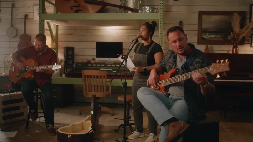 Singer sings from song sheet while musicians play guitars in a music room