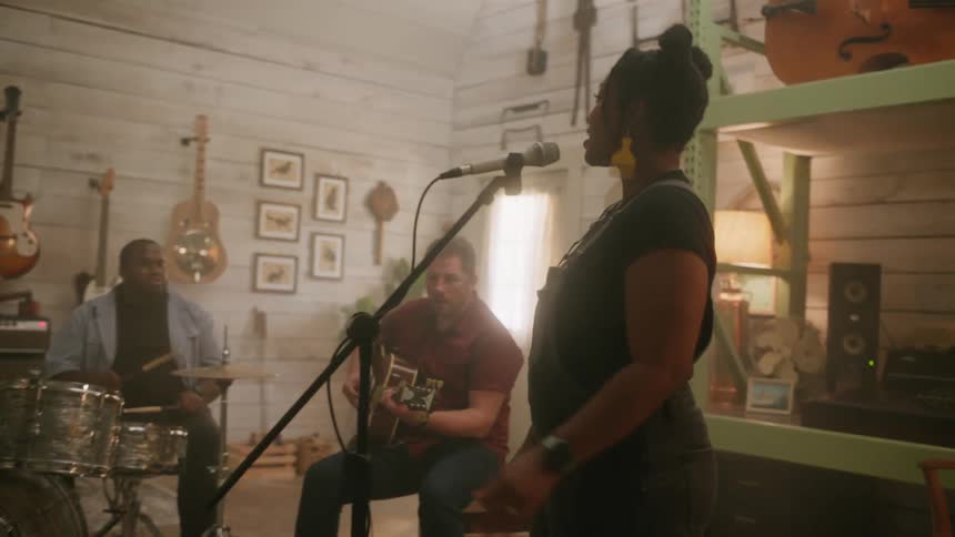 A cozy intimate music session is taking place in a warmly lit rustic room with a drummer guitarist and singer performing together