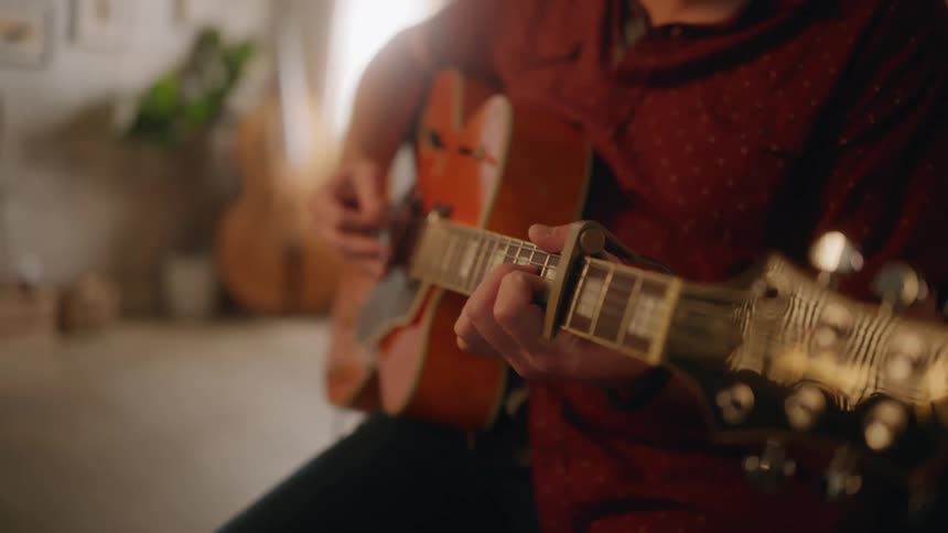Male guitarist plays electric guitar while sitting in music room