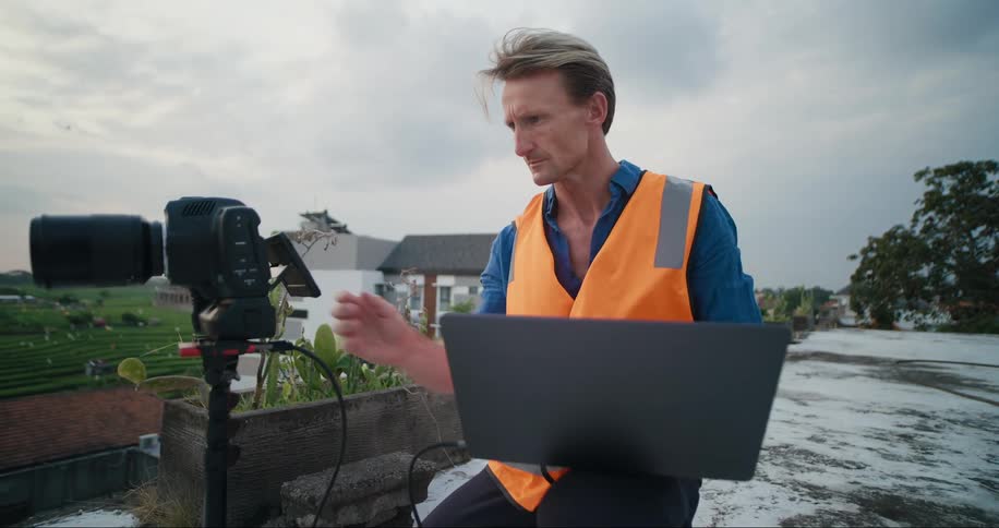 A man is taking photographs while using a laptop outside