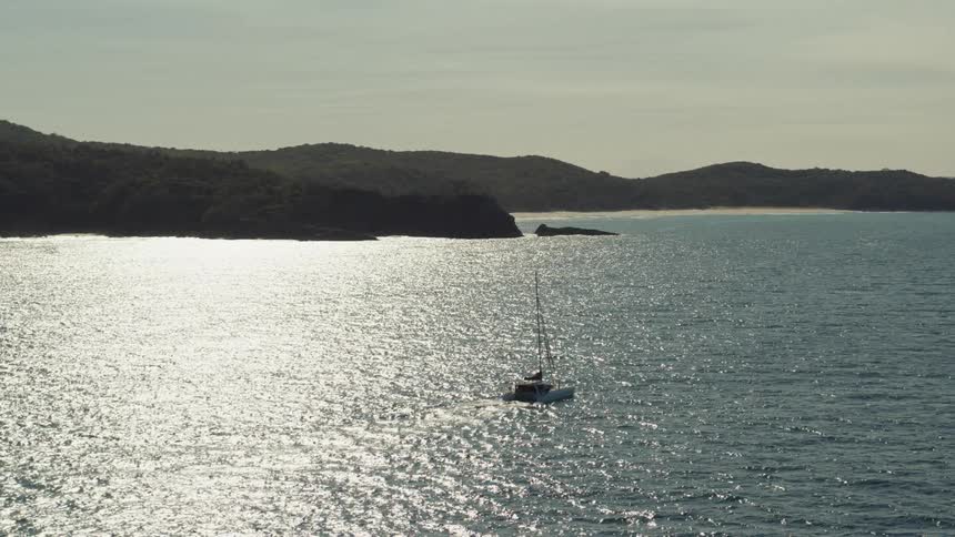 Yacht isolated in a vast ocean with the wooded coast in the background