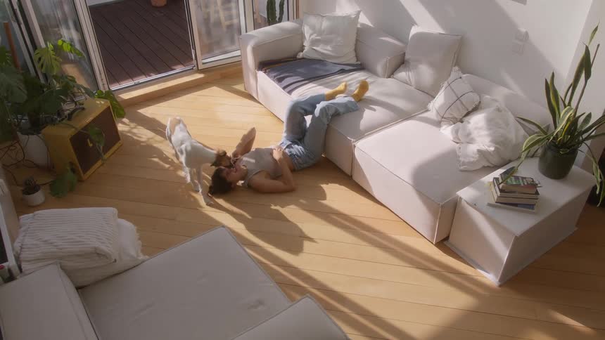 A person lies on the floor next to a white couch talking on the phone