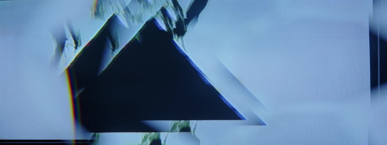 Black smudges flow through flickering triangles on a pale background