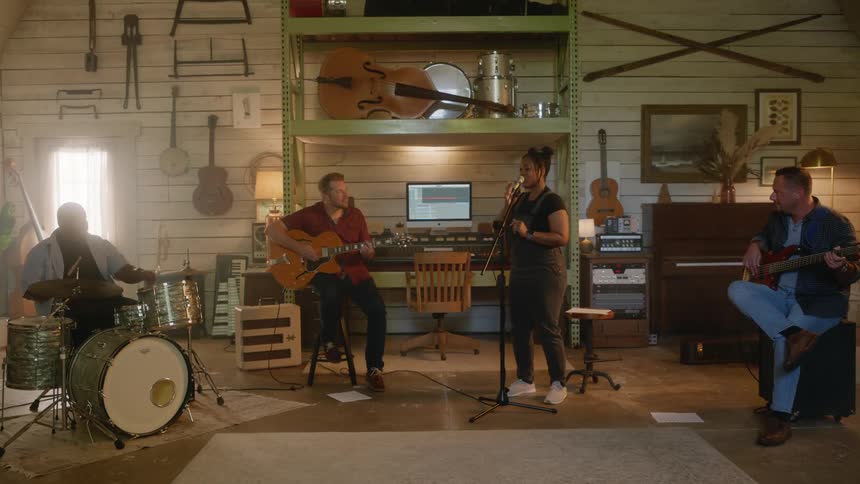 Musical band including drummer, guitarist, bassist, and vocalist singing and playing in a studio