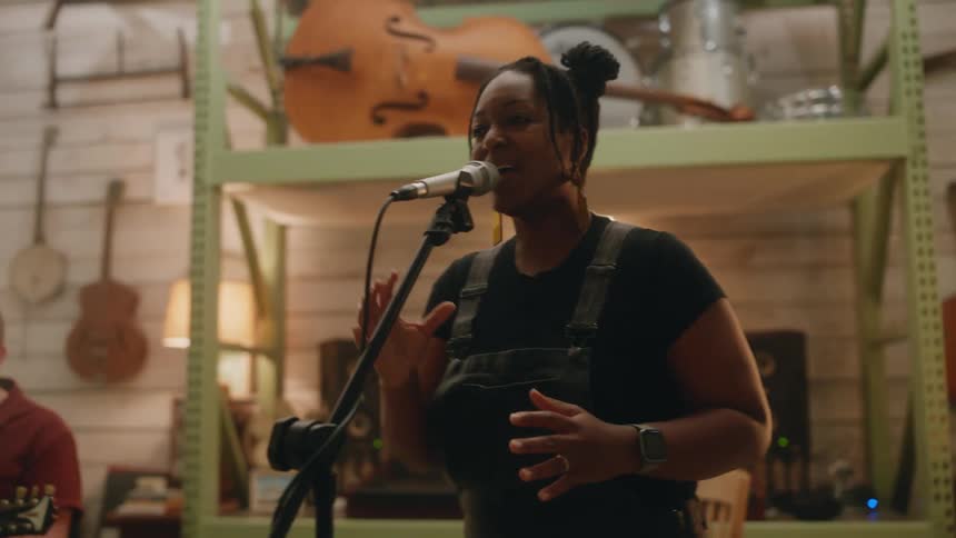 A black woman sings into a microphone in a music studio