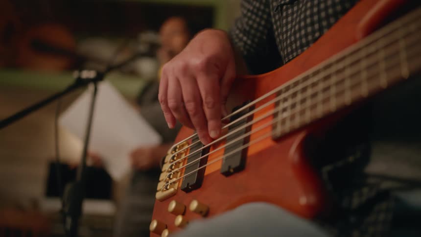 A singer sings a song in a recording studio with a musician playing a bass guitar in the foreground
