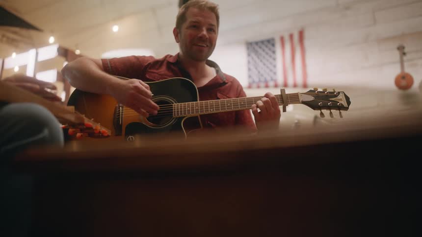A man strums a guitar while sitting in a room