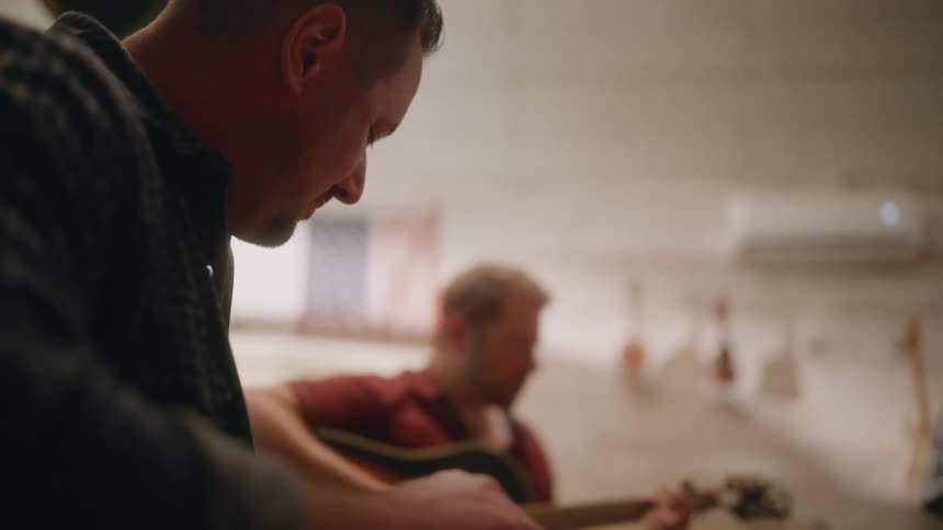 Two male guitarists sit together playing guitars