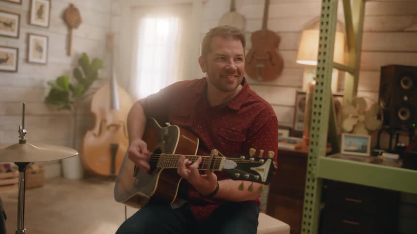 A man sitting on a stool is playing an acoustic guitar and moving his head to the music