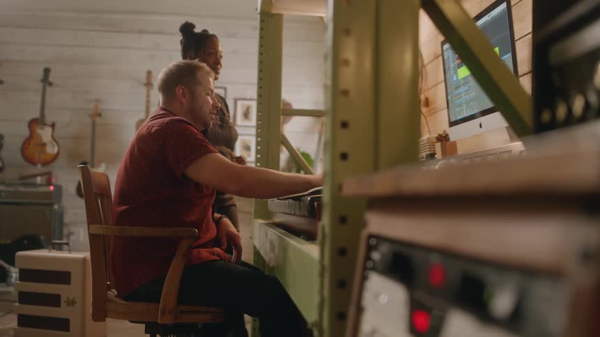 Two musicians talk while working on a sound board in a studio