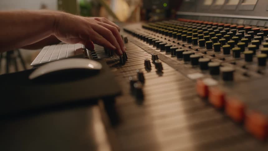 A man adjusting knobs on a mixing board in a recording studio
