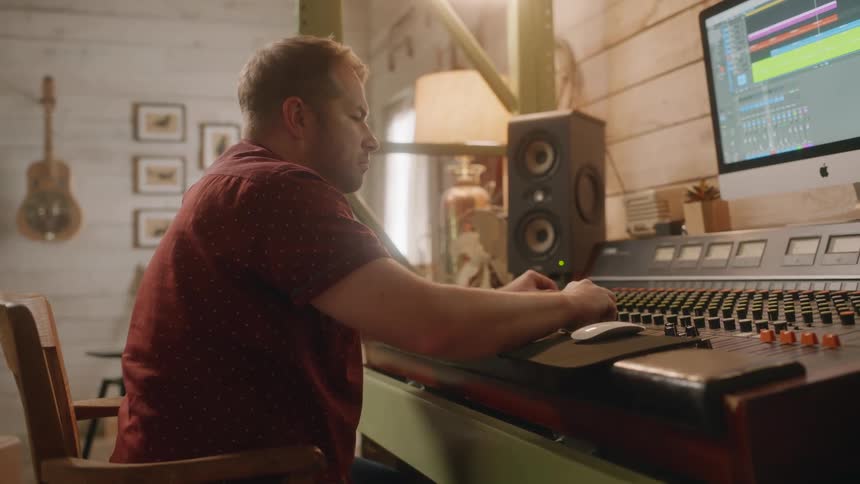 Sound engineer watching computer display adjusts setting on audio board
