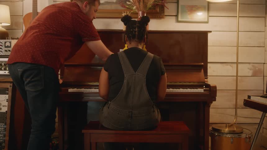 Sound engineer discusses details with a female musician sitting at a piano