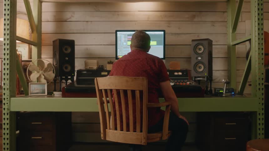 Man sitting in a chair working on a mixer in a music studio