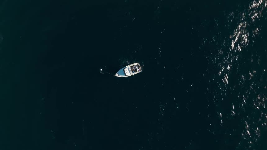 An aerial view reveals a small white boat with a blue hull anchored in a clear blue ocean